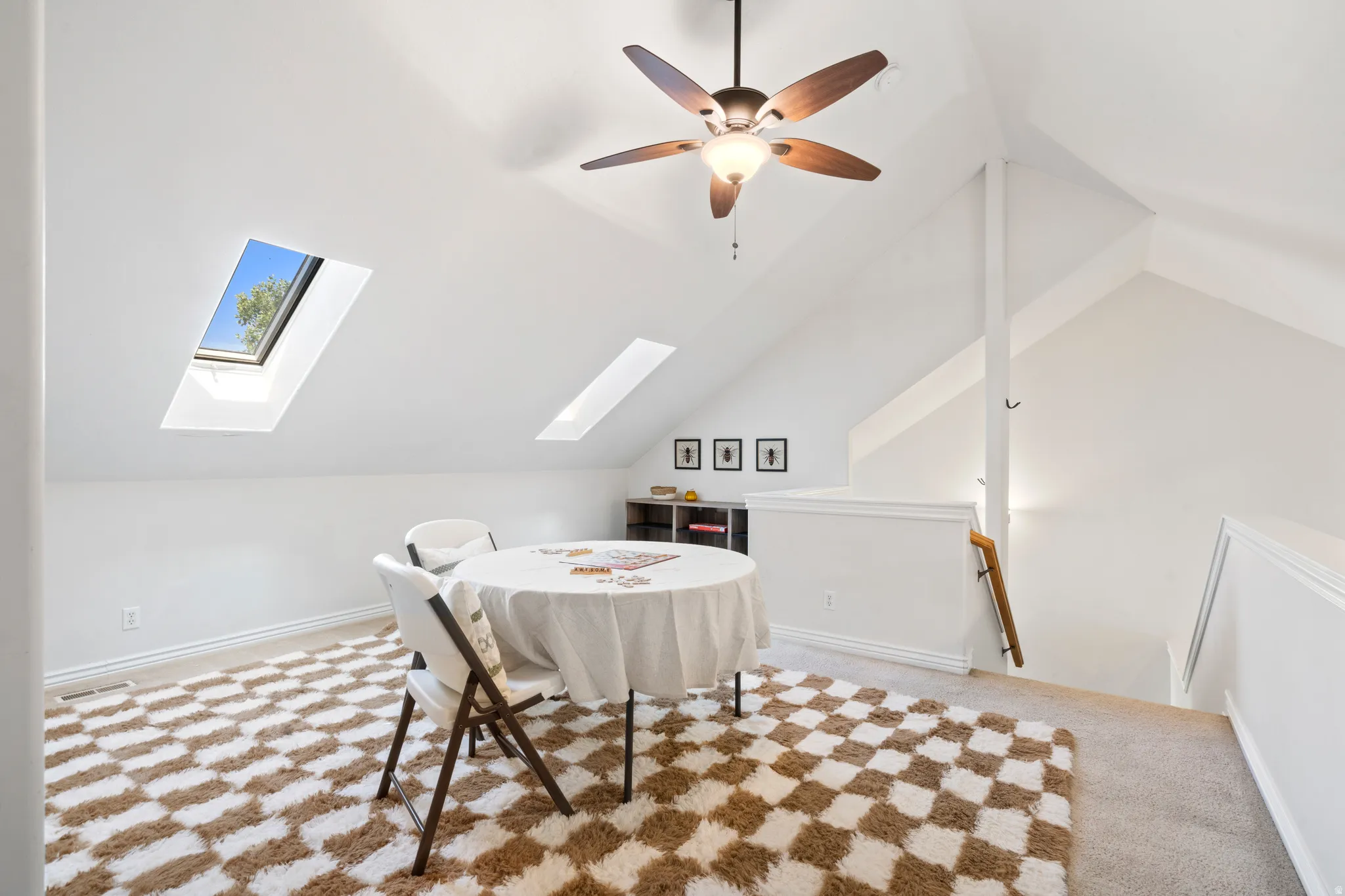 Bright loft space featuring a wood-finish ceiling fan, two skylights, a low wall partition, and a built-in shelving unit