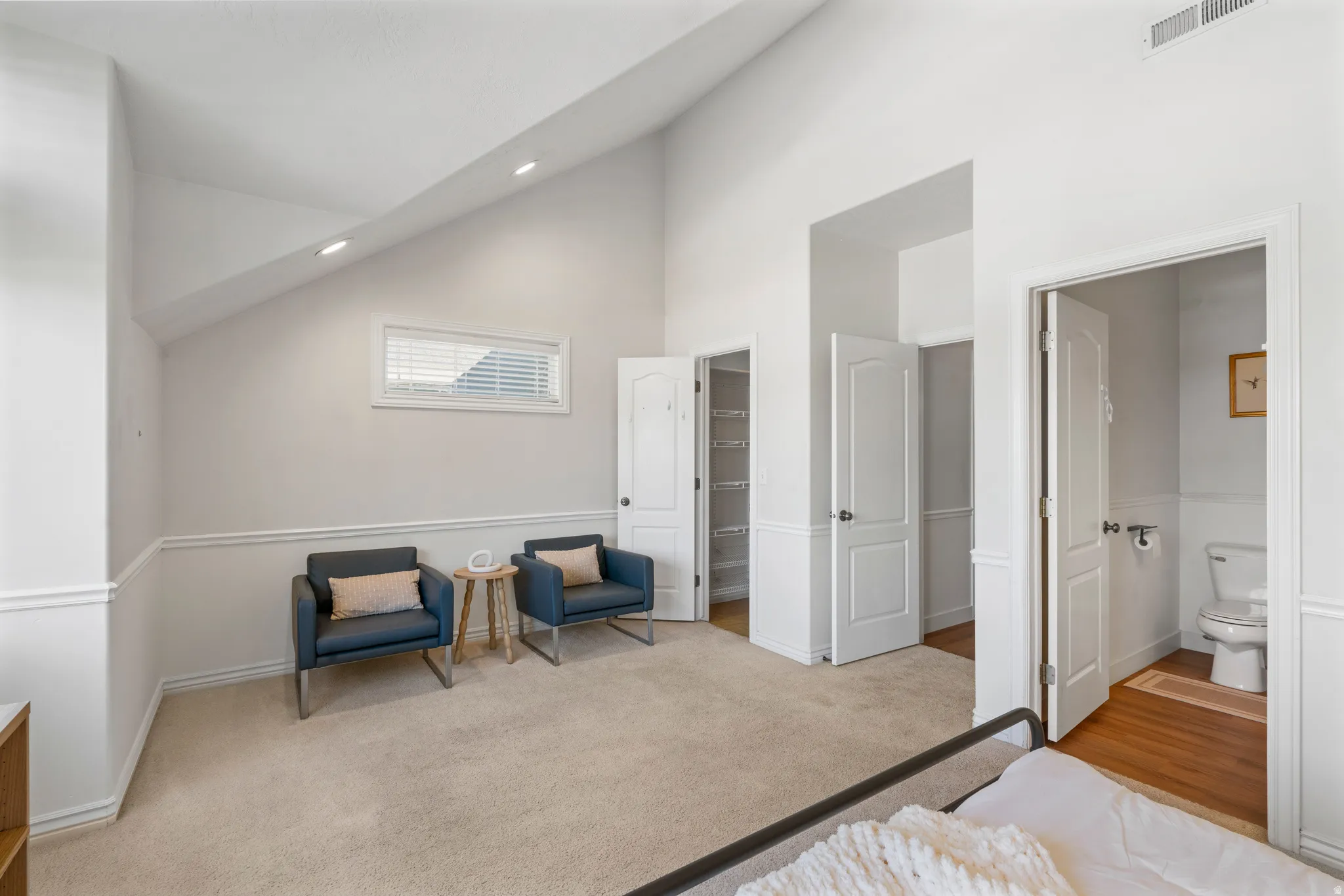 Vaulted ceiling with recessed lighting, beige carpet, horizontal window with blinds, white paneled doors, and wainscoting