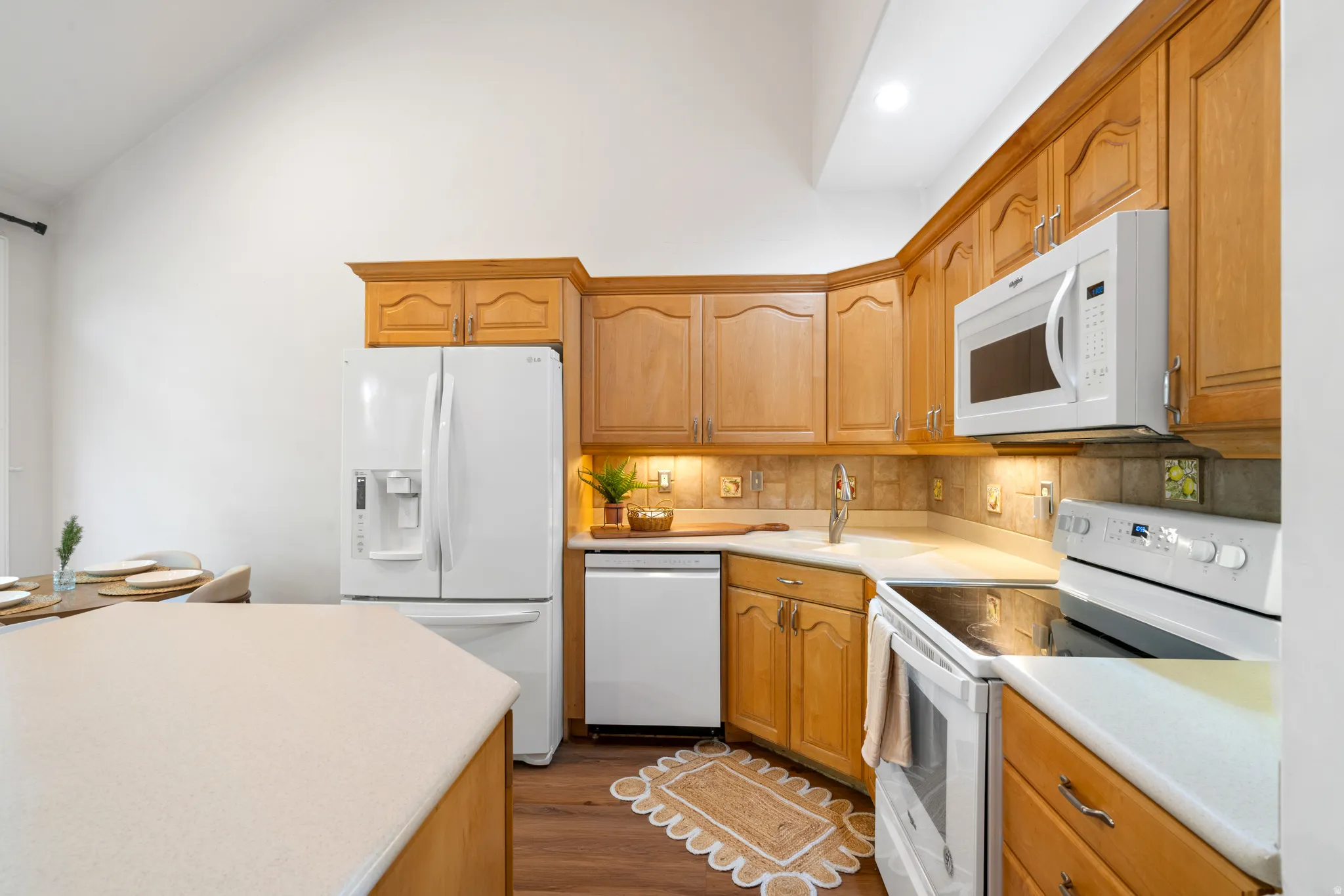 Kitchen featuring light wood cabinetry, white appliances, solid surface countertops, and a tile backsplash