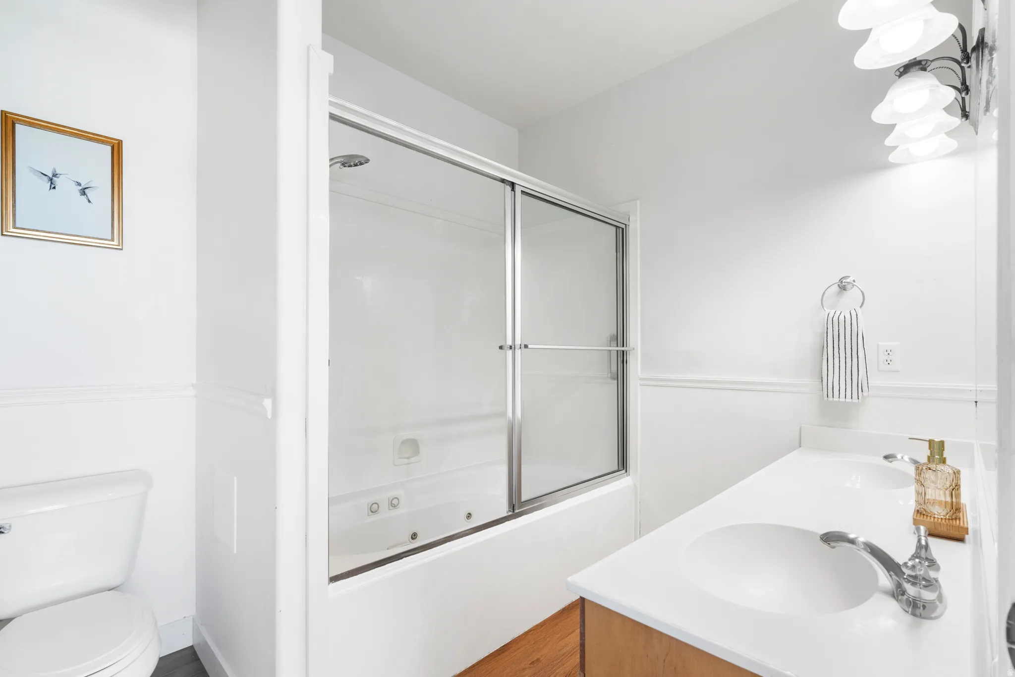 Bathroom featuring a white bathtub with sliding glass doors, a vanity with dual integrated sinks, and a toilet