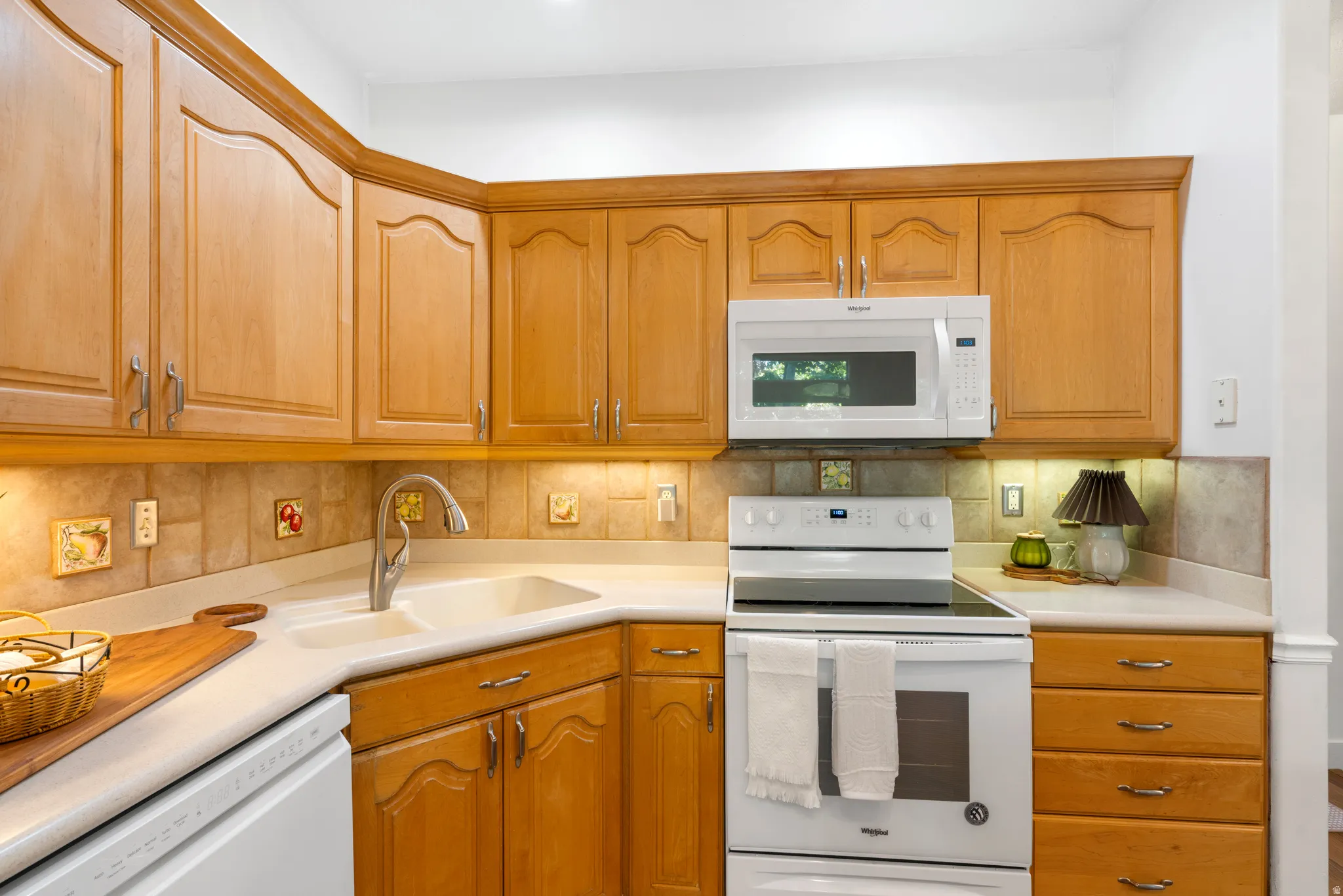 Kitchen featuring wood cabinetry, solid surface countertops, tile backsplash, and integrated appliances including a white electric range, microwave, and dishwasher