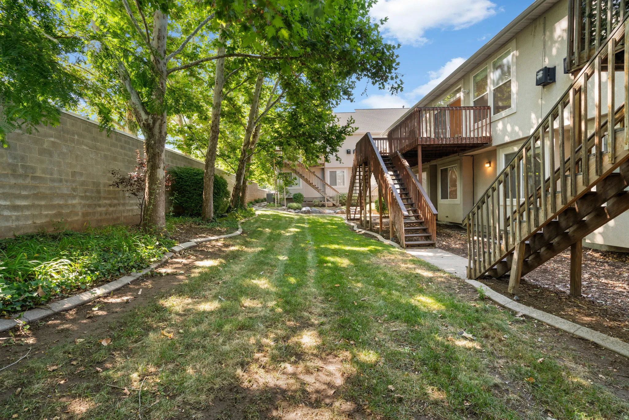 Expansive grass lawn featuring mature trees and a block privacy wall