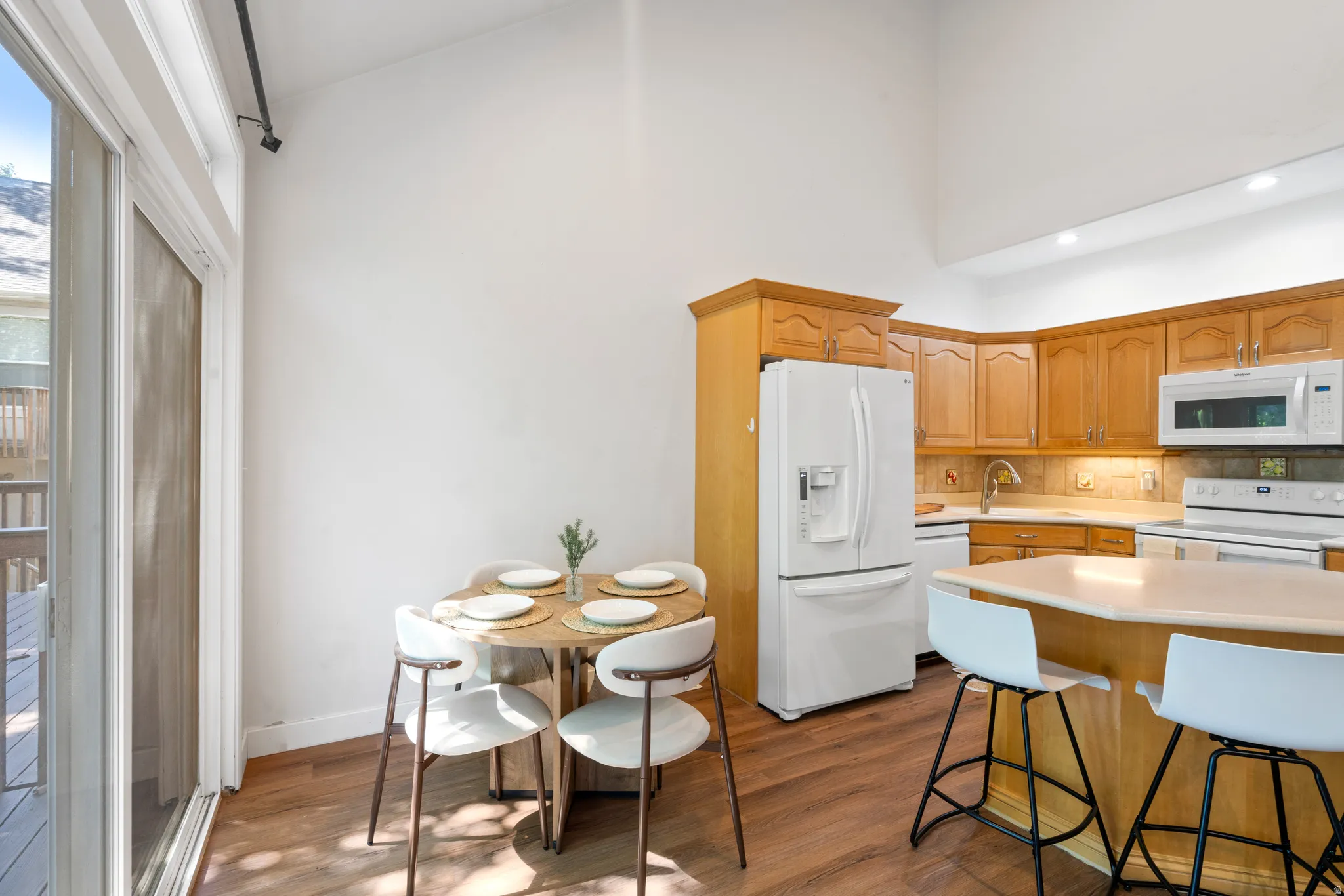 Vaulted ceiling kitchen featuring wood-finish flooring, light wood cabinetry, a built-in kitchen island with seating, and a sliding glass door providing exterior access