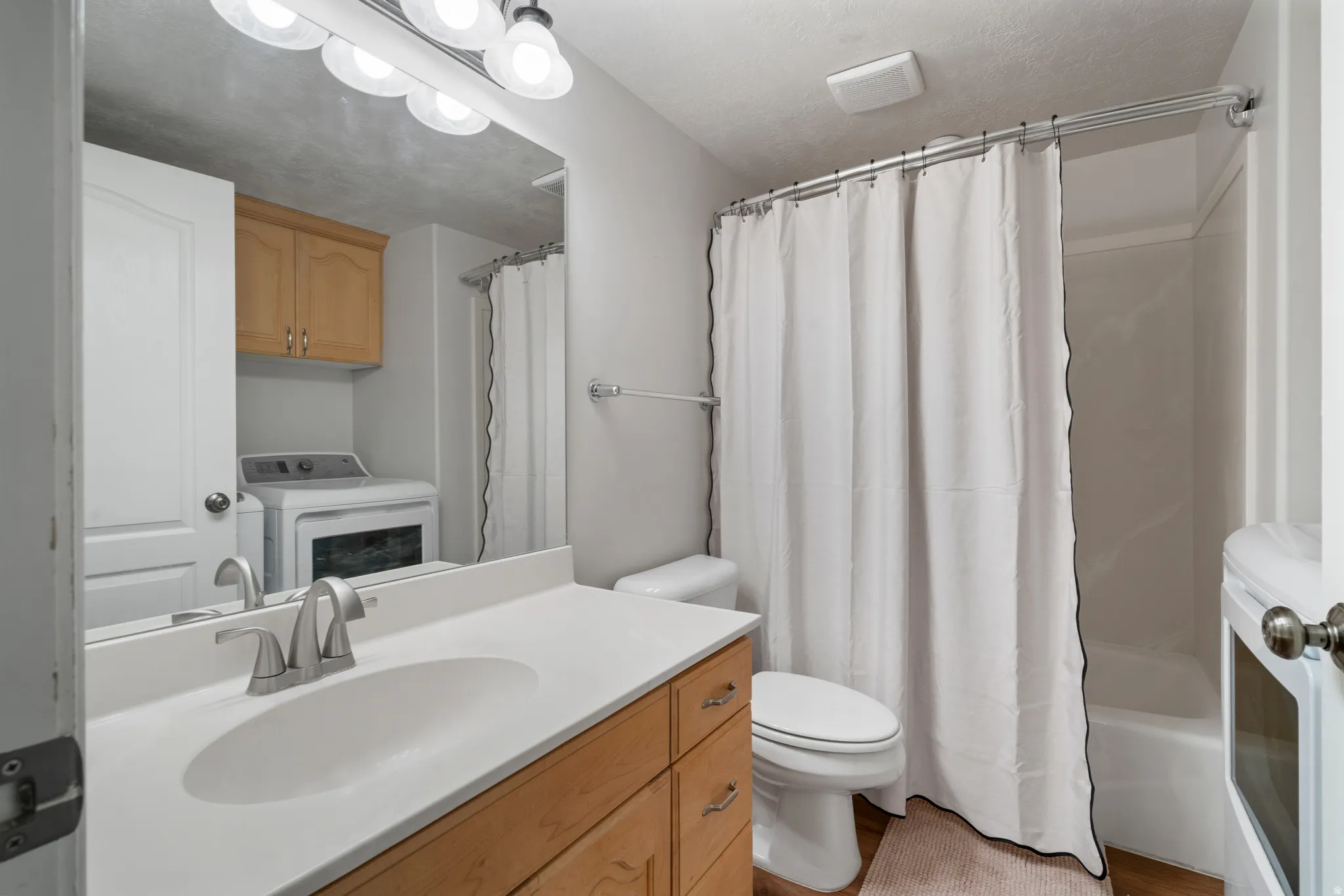 Bathroom featuring a vanity with a white countertop and a single basin, brushed nickel faucet, light wood cabinetry, and a shower-over-tub combination with a white shower curtain