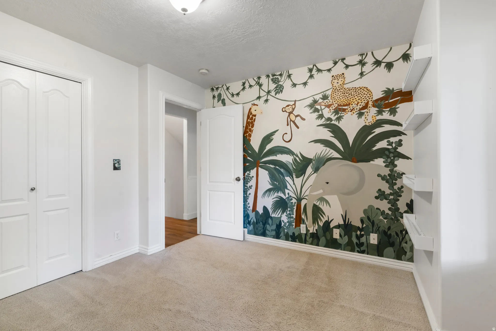 Bedroom featuring a statement accent wall with a jungle mural, light-toned carpeting, white trim, and a ceiling-mounted light fixture