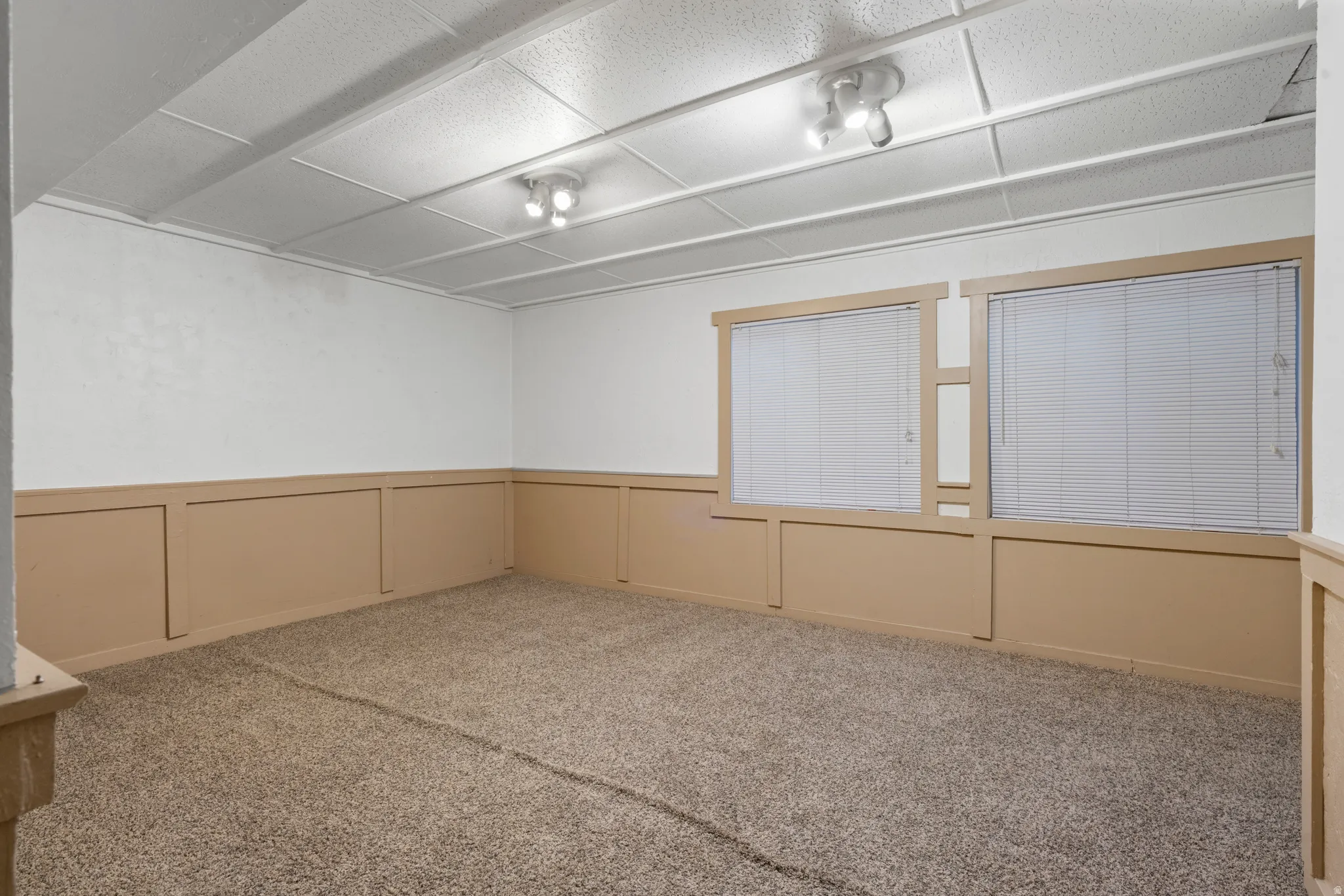 Carpeted room featuring two windows with horizontal blinds, board and batten style wainscoting, white walls, and a drop ceiling with recessed lighting