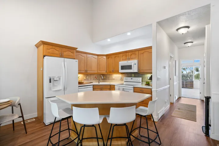 Kitchen featuring wood-finish flooring, light wood cabinetry, white appliances, and a central island with countertop seating