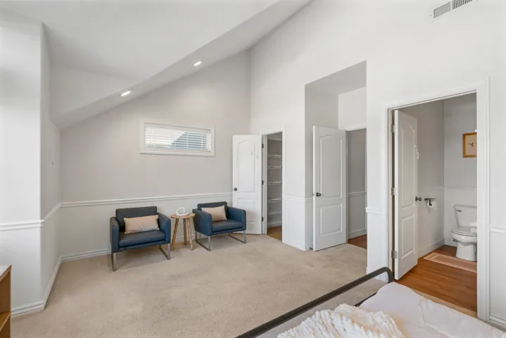 Vaulted ceiling with recessed lighting, beige carpet, horizontal window with blinds, white paneled doors, and wainscoting