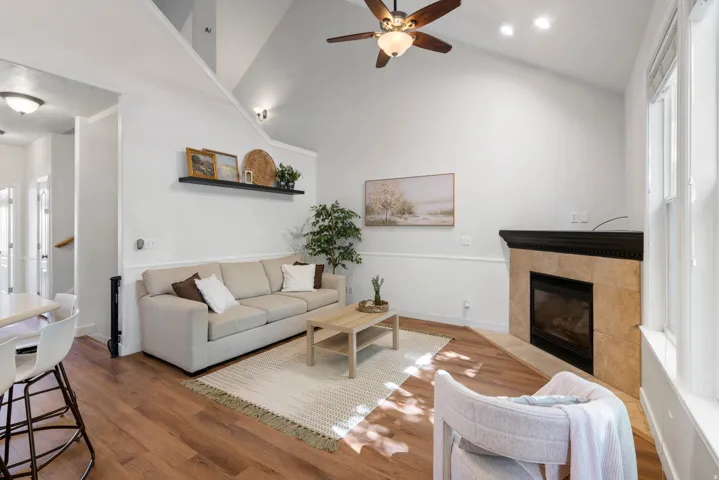 Living area featuring vaulted ceilings, wood-finish flooring, a ceiling fan, and a fireplace with a tile surround and dark wood mantel