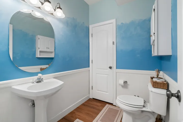 Pedestal sink with chrome faucet, circular mirror, and three-light vanity fixture