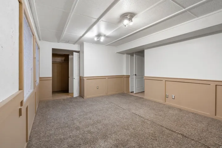 Expansive room featuring neutral carpeting, white and tan two-tone wall paneling, and an exposed beam ceiling with recessed lighting fixtures
