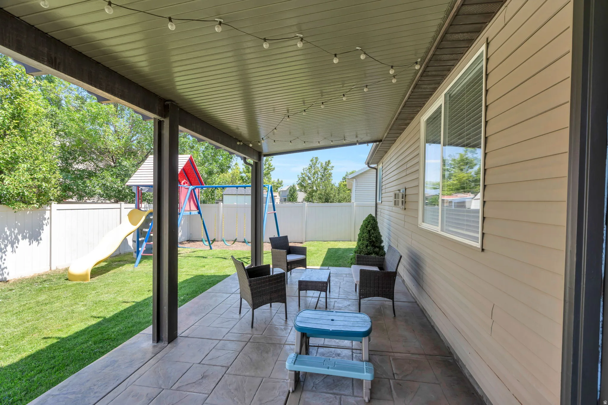 Covered patio with tile flooring and overhead track lighting, opening directly to a level lawn with mature landscaping