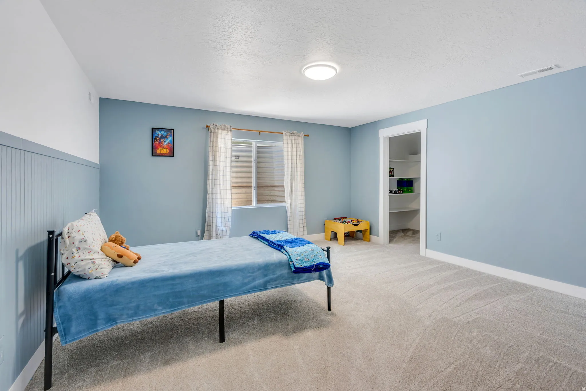 Carpeted room featuring a window with horizontal blinds, a ceiling-mounted light fixture, white trim, and a built-in closet with shelving