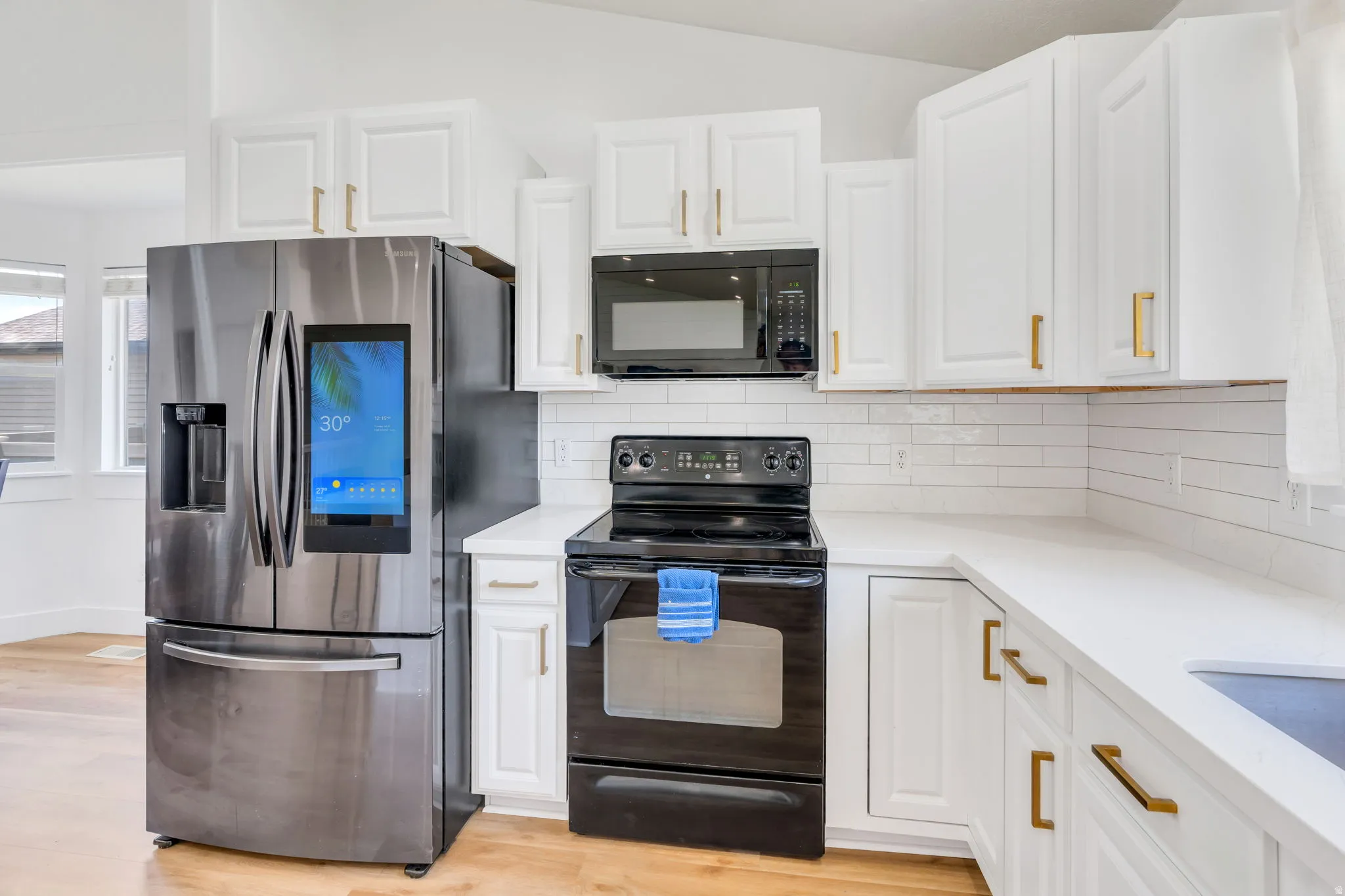 Modern kitchen featuring a stainless steel French door refrigerator, white shaker-style cabinetry with gold-tone hardware, and light-toned countertops