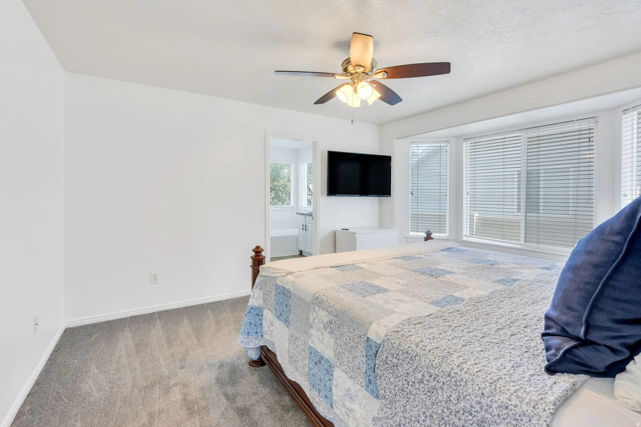 Bedroom featuring a bay window, ceiling fan with integrated lighting, carpet flooring, and a doorway opening to an additional space