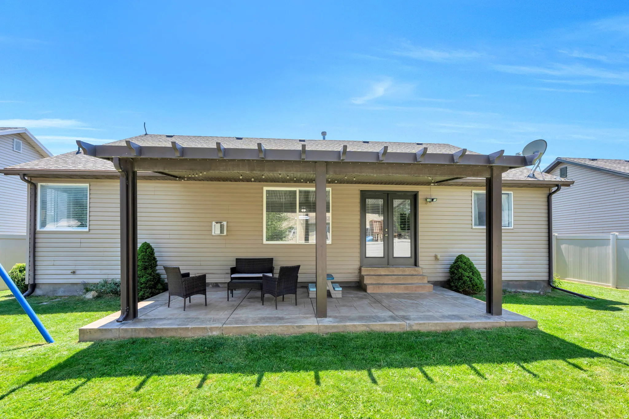 Covered patio with pergola overhead and black metal seating arrangement overlooking a manicured lawn