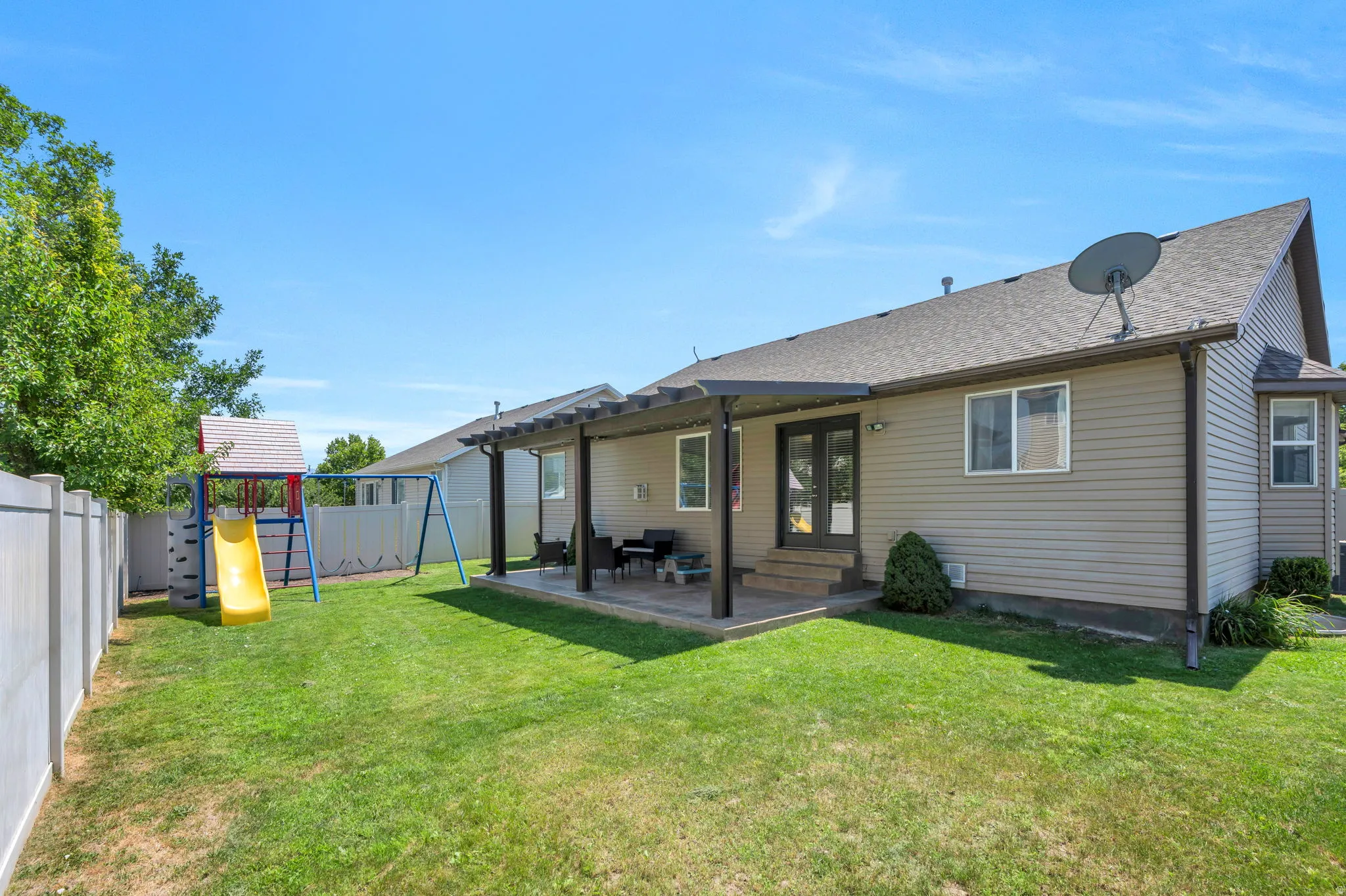 Spacious backyard oasis featuring a manicured lawn, covered patio with ceiling fans, and mature landscaping