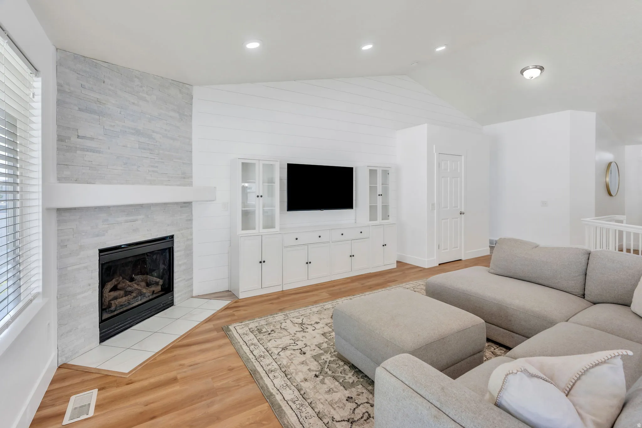 Living area featuring a stone-faced fireplace with white mantel, built-in media cabinetry, wood-finish flooring, and recessed lighting