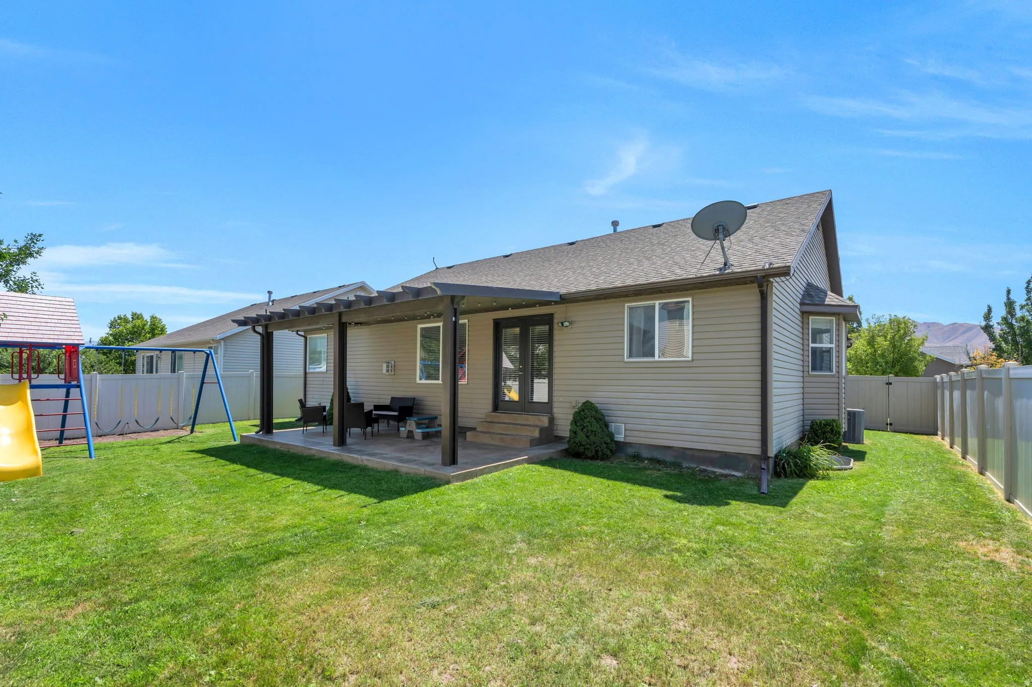 Expansive backyard featuring a pergola-covered patio, green lawn, vinyl siding, and a privacy fence
