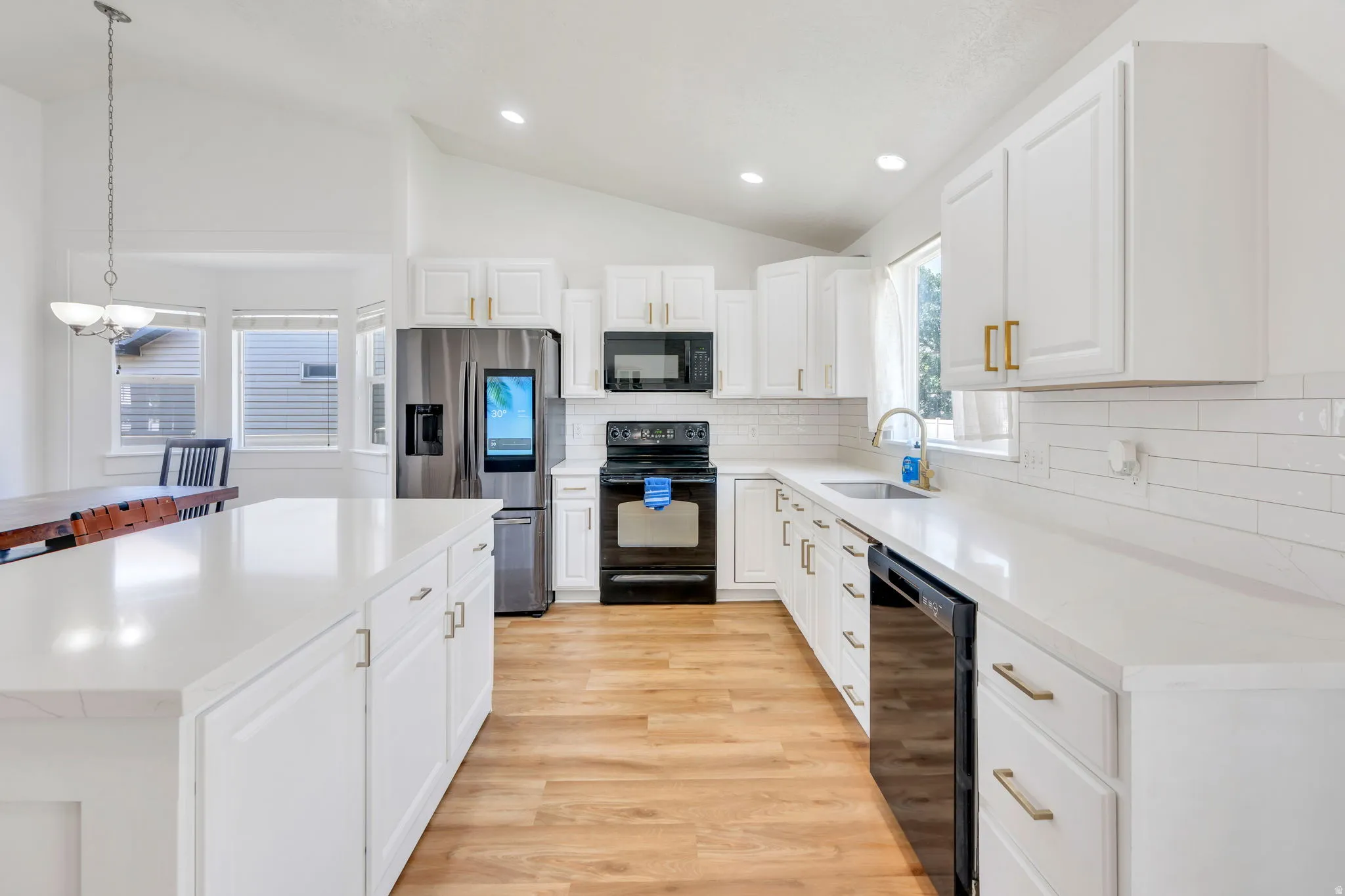 Kitchen featuring white cabinetry, light-toned countertops, wood-finish flooring, a full suite of black and stainless steel appliances, and a white subway tile backsplash
