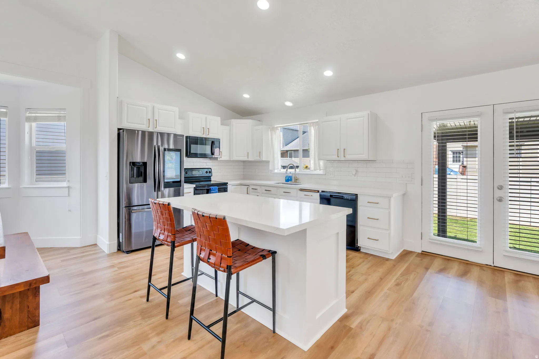 Bright kitchen featuring a central island, white cabinetry, stainless steel appliances, wood-finish flooring, and double glass-paneled doors