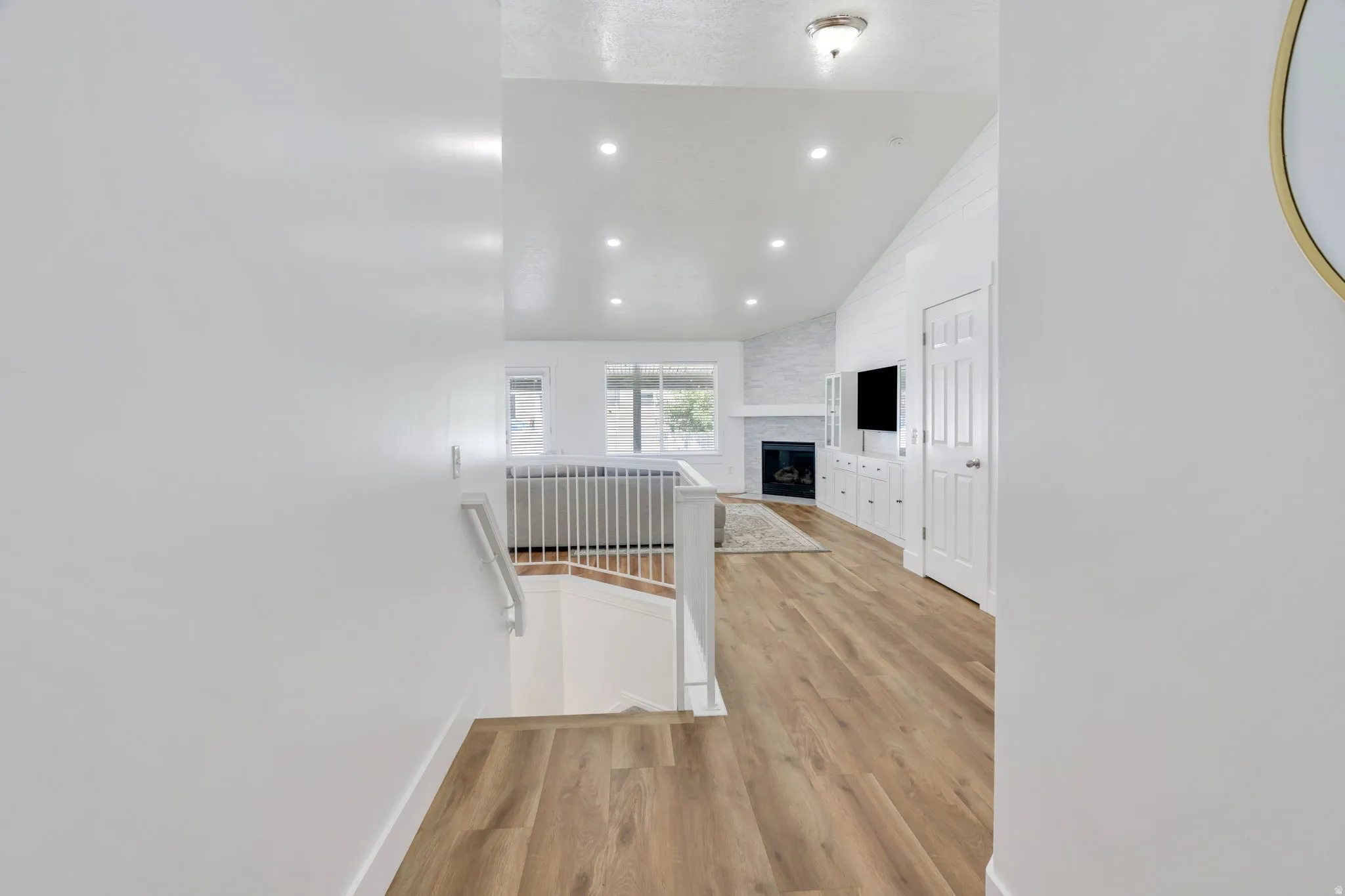 Open-concept upper-level landing featuring wood-finish flooring throughout, recessed ceiling lighting, white painted walls, and a metal stair railing