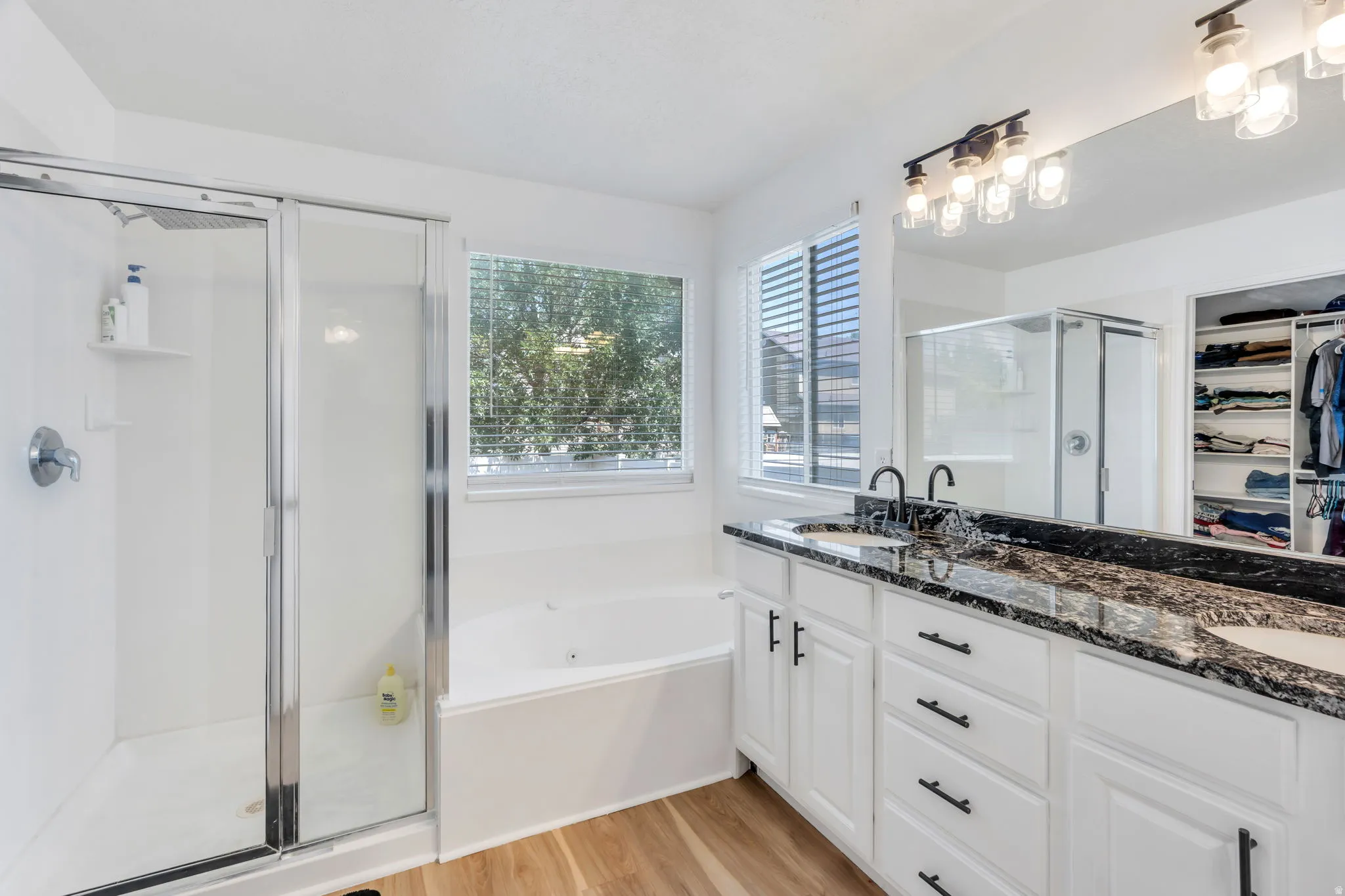 Bathroom featuring a dual vanity with a dark granite countertop, white cabinetry with matte black hardware, and a large mirror with a multi-bulb light fixture