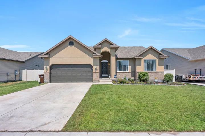 Welcoming curb appeal defines this single-story residence, featuring a stucco exterior in warm neutral tones, peaked rooflines with architectural detail, and a dark-finish garage door