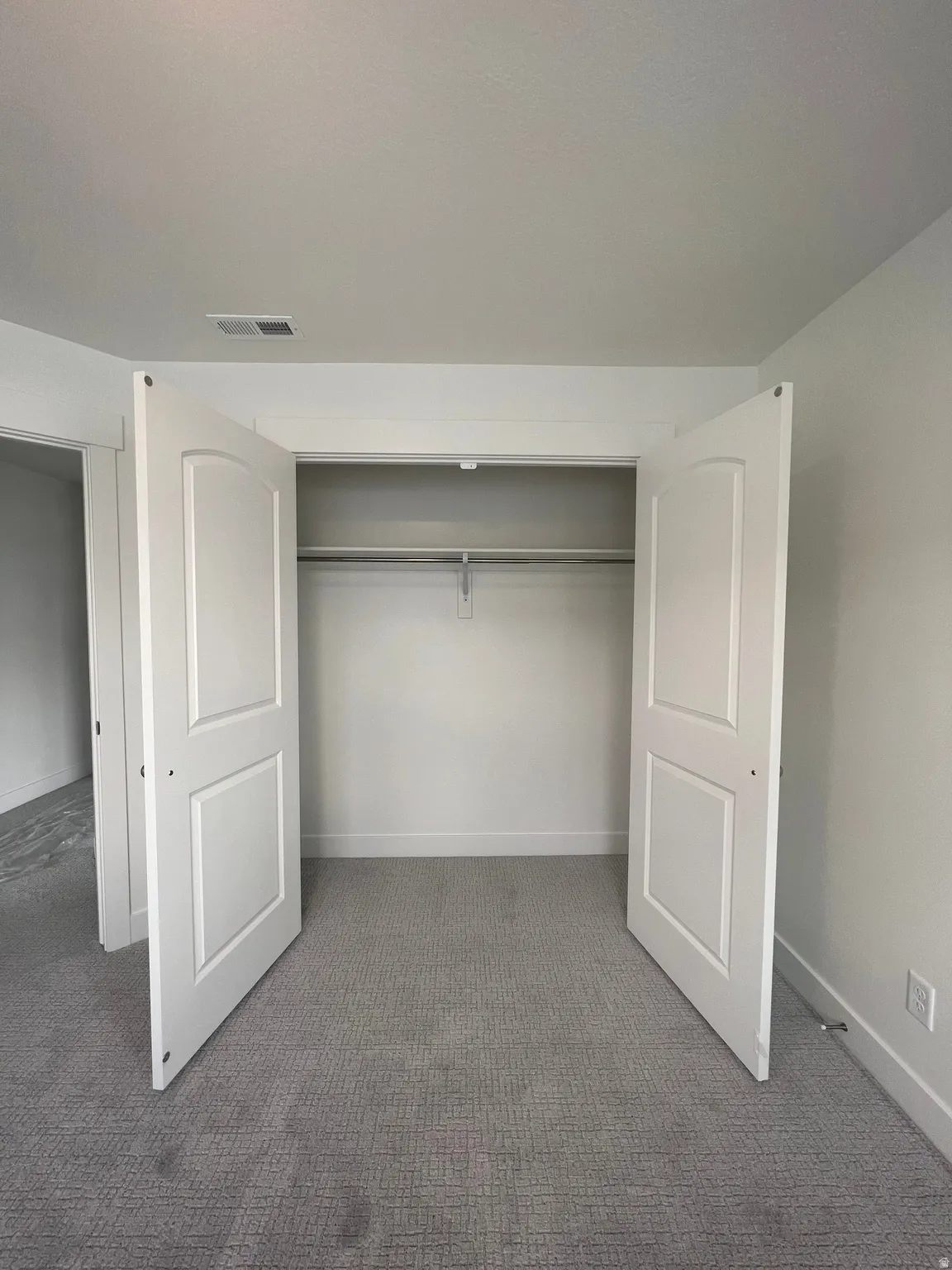 Closet with white bi-fold doors, single clothes rod, and overhead shelving