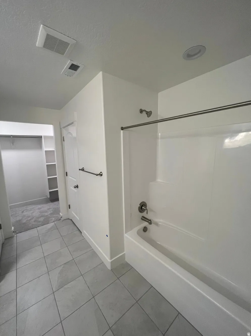 Spacious primary bathroom featuring a tile-lined floor, recessed ceiling lighting, and a bathtub-shower combination with sliding glass enclosure and chrome fixtures
