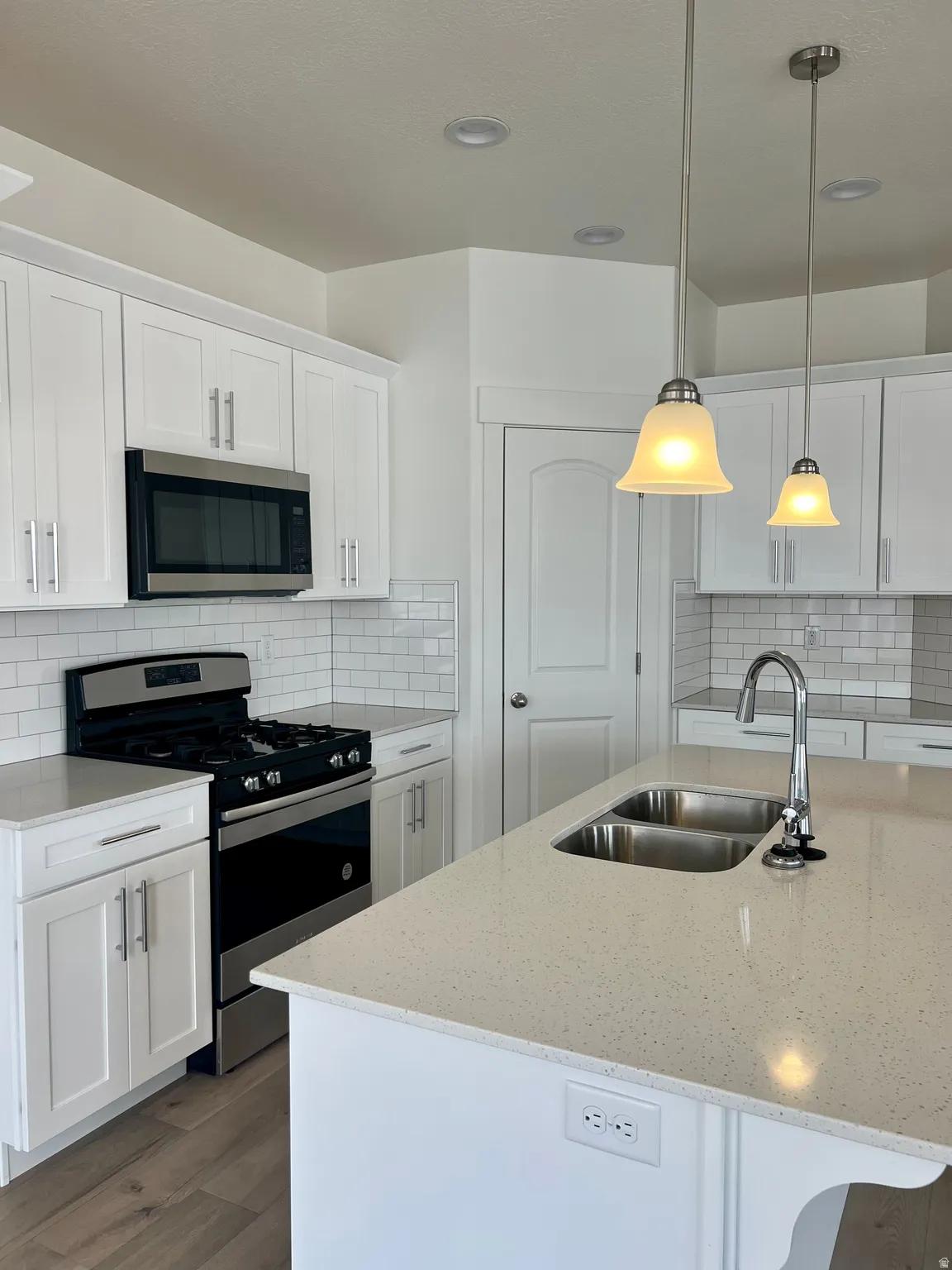 Contemporary kitchen featuring white shaker cabinetry, light-toned countertops, a stainless steel gas range, and a subway tile backsplash