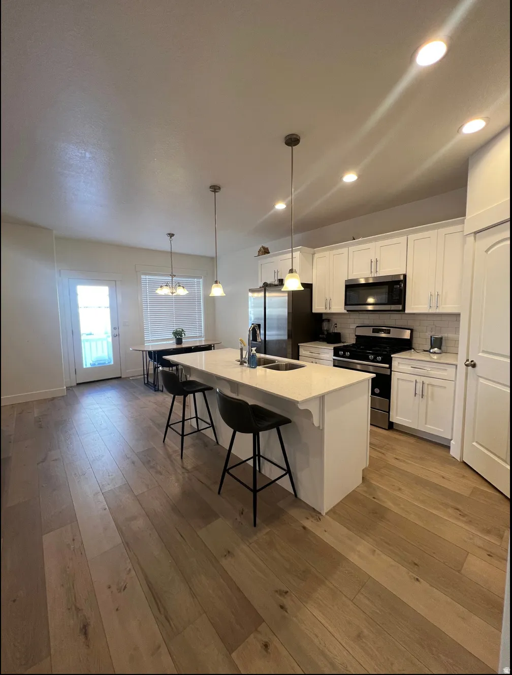 Open concept kitchen featuring an eat-at island with pendant lighting, white cabinetry, and stainless steel appliances