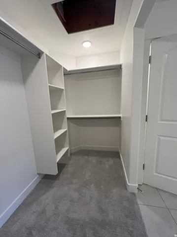 Walk-in closet featuring built-in shelving, dual hanging rods, recessed ceiling light, and gray patterned carpeting