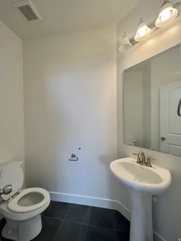 Pedestal sink featuring a brushed nickel faucet, framed mirror, and a three-light vanity fixture