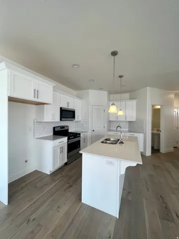 Kitchen featuring an expansive center island with an undermount sink, white shaker-style cabinetry, stainless steel appliances, light wood-finish flooring, and subway tile backsplash