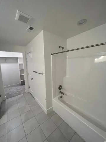 Spacious primary bathroom featuring a tile-lined floor, recessed ceiling lighting, and a bathtub-shower combination with sliding glass enclosure and chrome fixtures