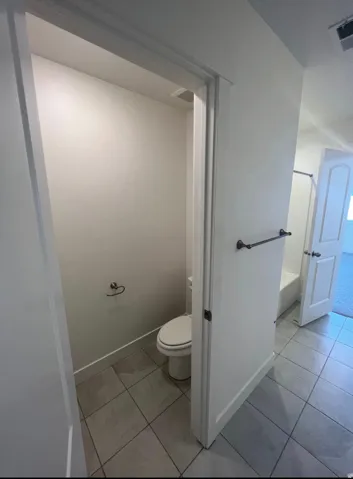 Tiled flooring bathroom featuring a toilet enclosure, white wall paint, and a towel bar