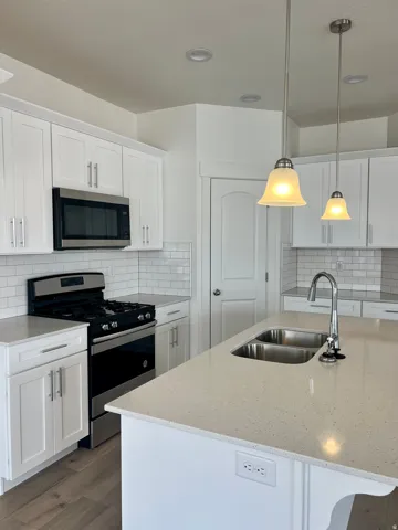 Contemporary kitchen featuring white shaker cabinetry, light-toned countertops, a stainless steel gas range, and a subway tile backsplash