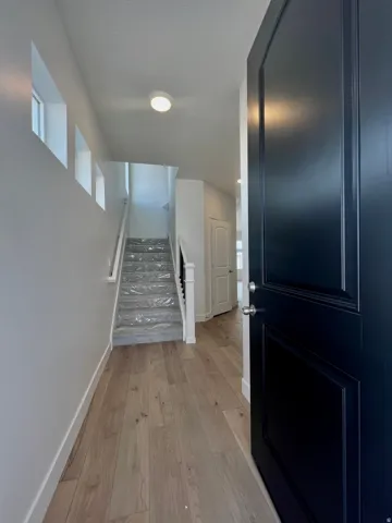 Entryway featuring wood-finish flooring, a contemporary dark paneled door with brushed nickel hardware, and an open staircase with white risers and handrail