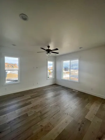 Spacious room featuring wide plank wood-finish flooring, recessed lighting, a ceiling fan, and multiple windows with white trim