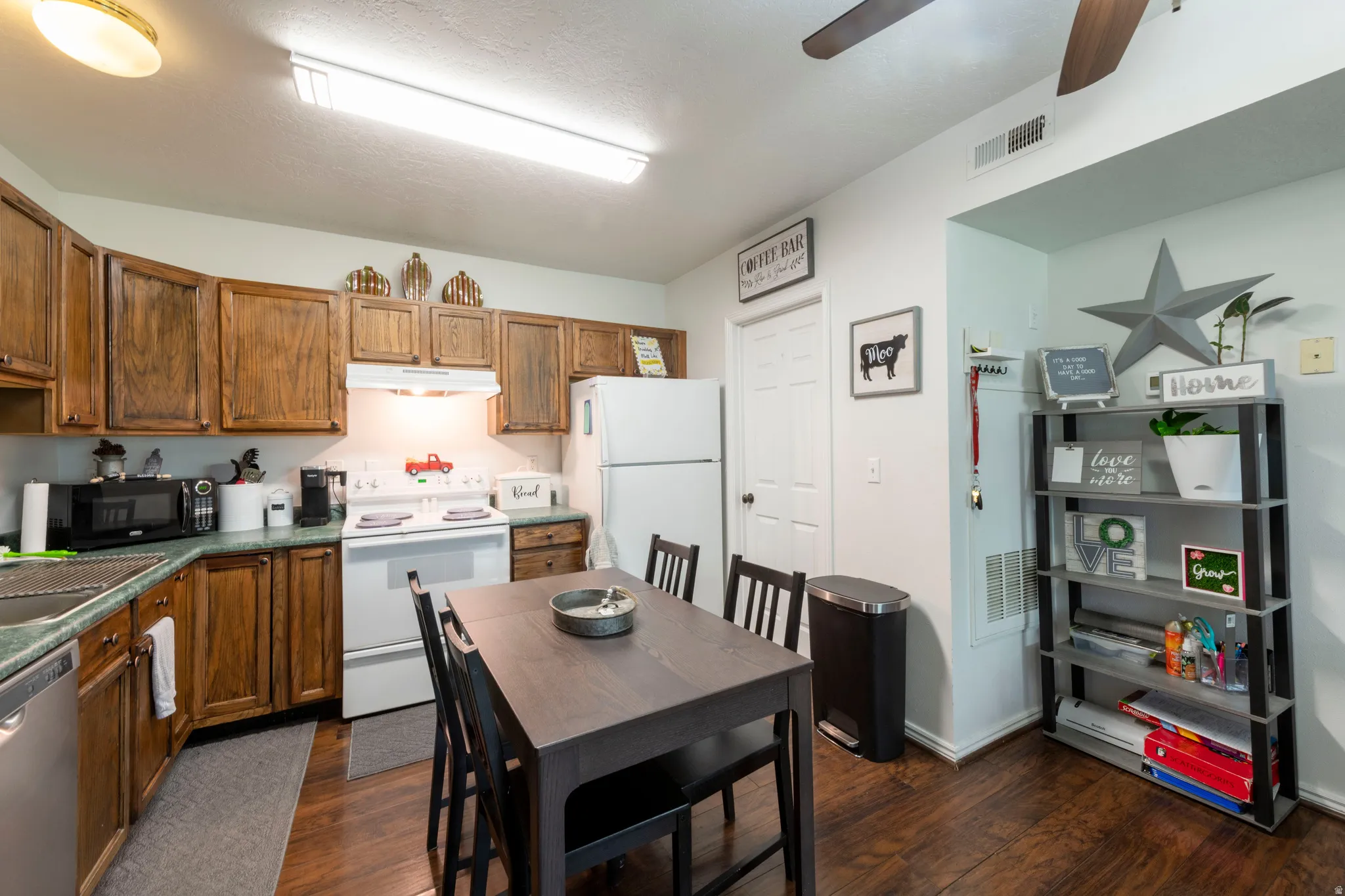 Kitchen area featuring wood-finish flooring, wood cabinetry, white appliances, and a ceiling fan