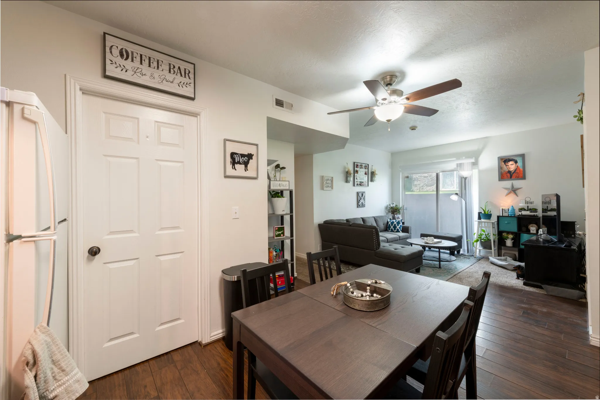 Open-concept living area featuring wood-finish flooring, a ceiling fan with integrated lighting, and a sliding glass door