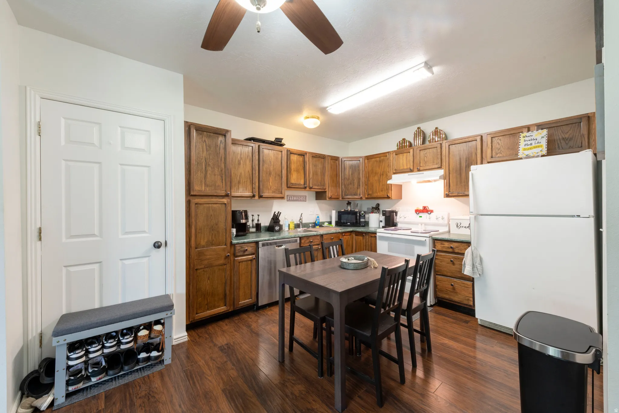 Functional kitchen with wood-finish flooring, wood cabinetry, a ceiling fan, and white appliances including a refrigerator and range