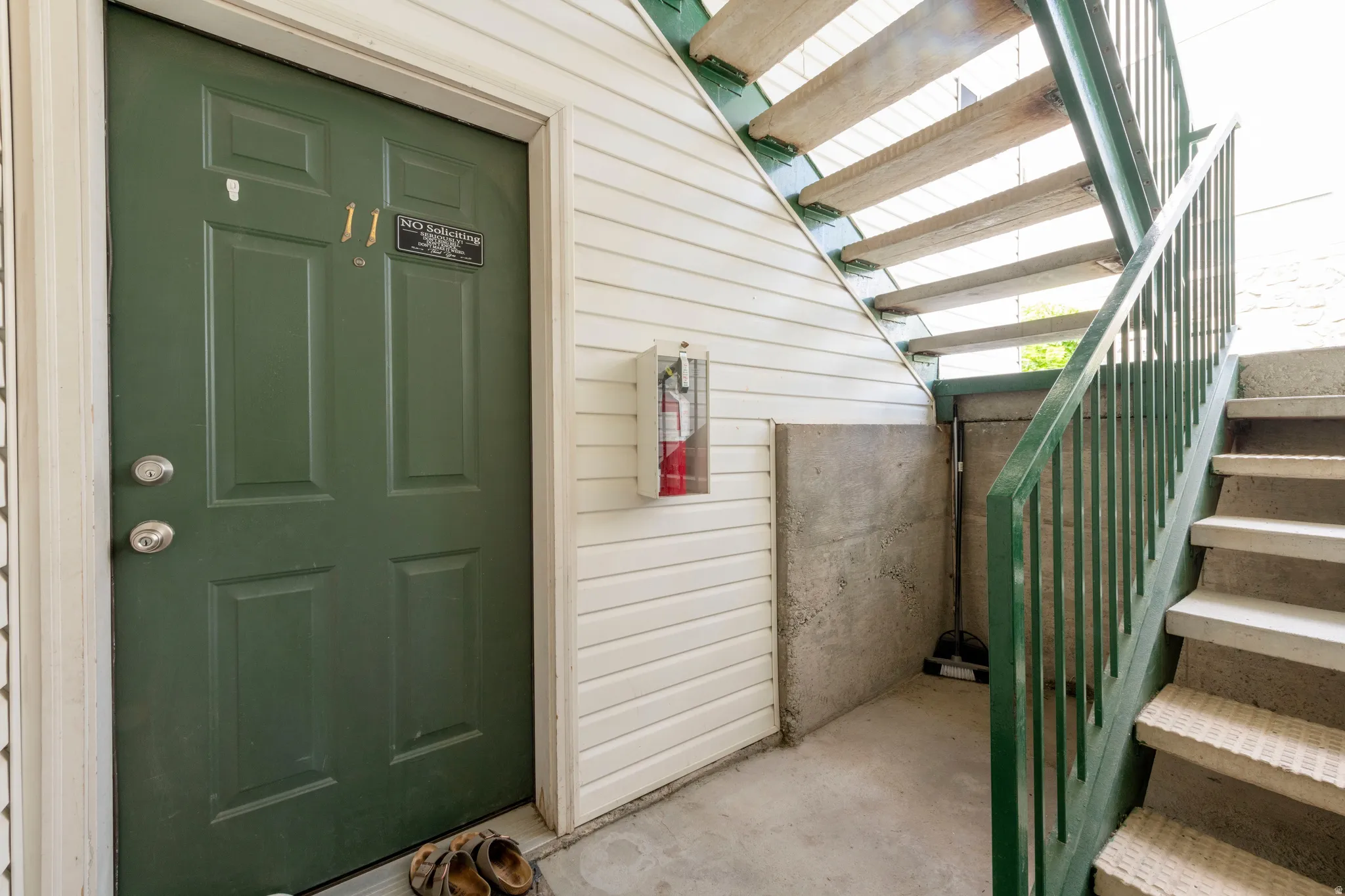 Entryway featuring a paneled green door with brushed nickel hardware, white siding, and concrete flooring