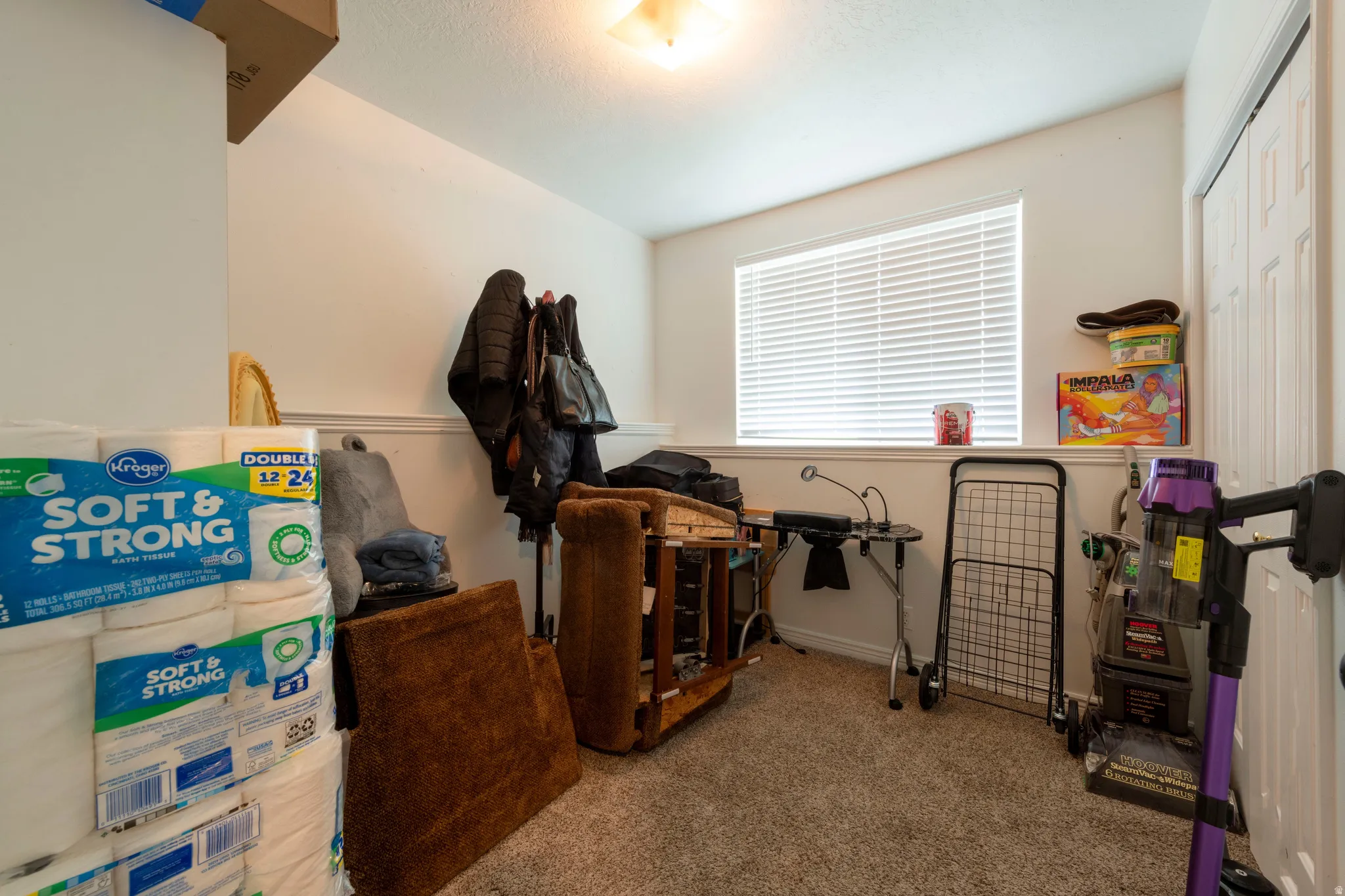 Carpeted interior room featuring a single window with horizontal blinds, neutral painted walls with chair rail molding, and a ceiling-mounted light fixture