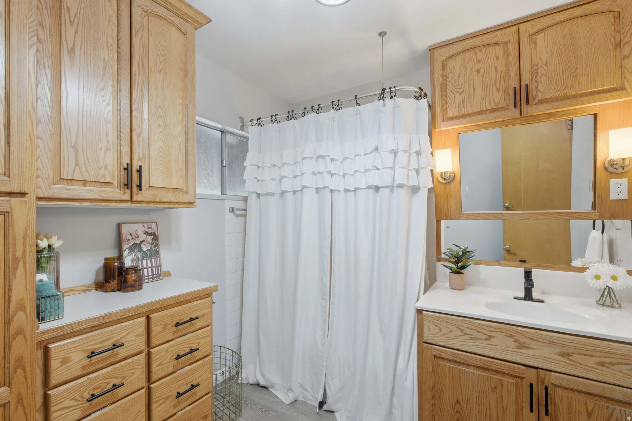 Bathroom featuring a wood-finish vanity with an integrated sink and matte black faucet, wall-mounted mirror with sconce lighting, and extensive wood-finish cabinetry