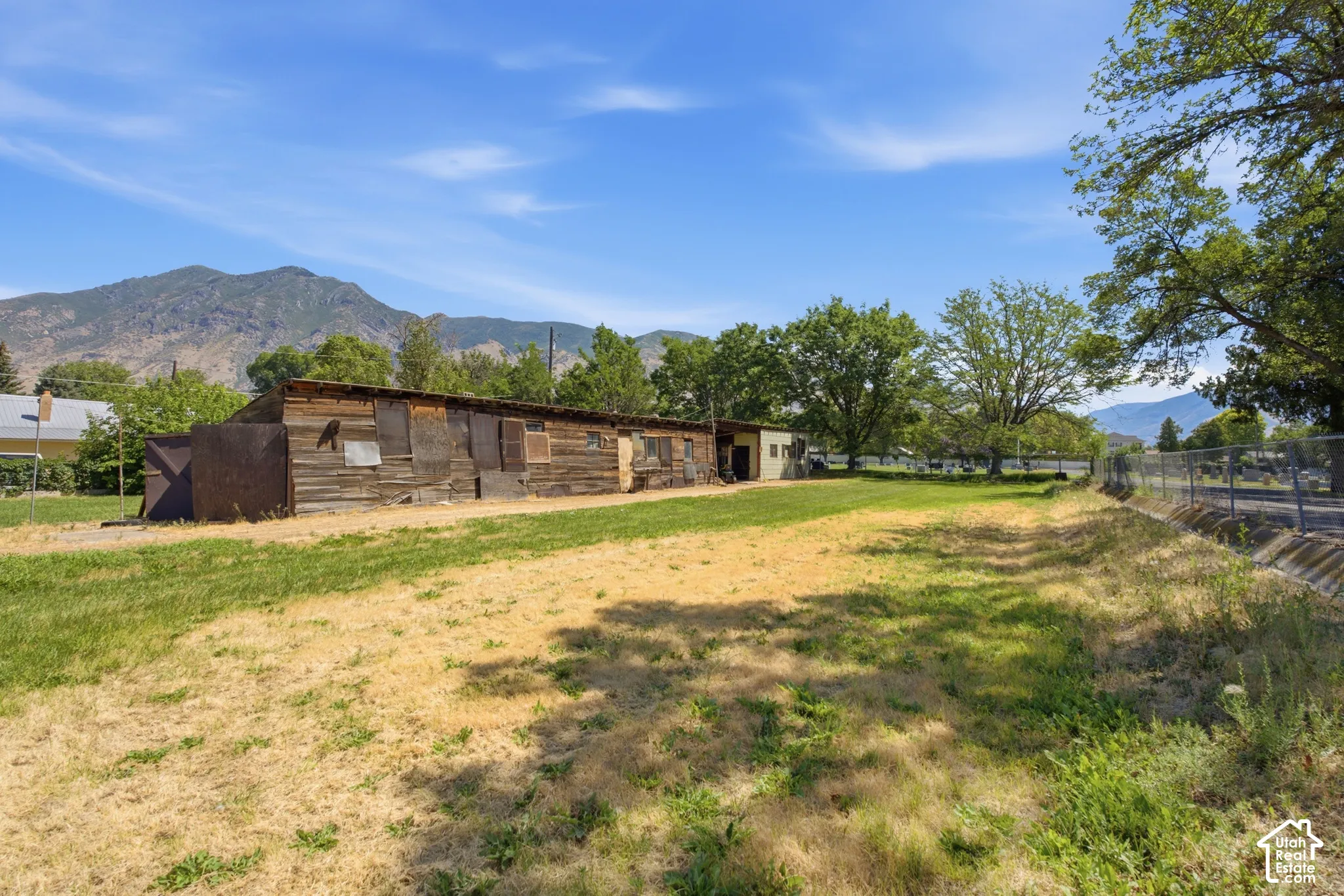 Expansive grassy lot with mature trees and mountain scenery