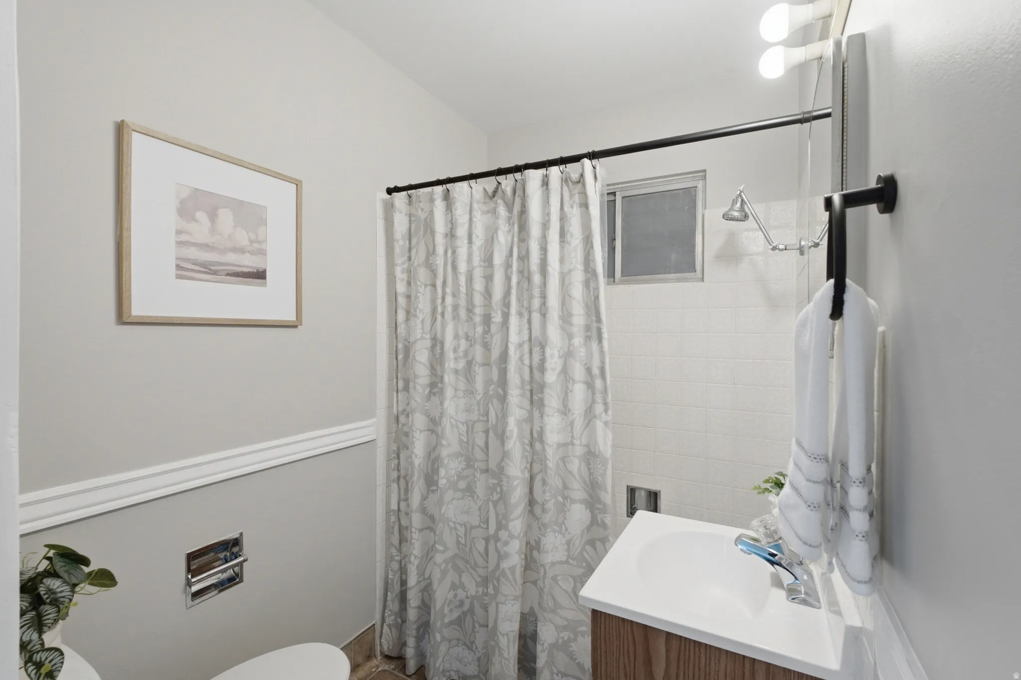 Bathroom featuring a wood-finish vanity with a white basin sink, a tiled shower with a window, and light gray walls with decorative molding