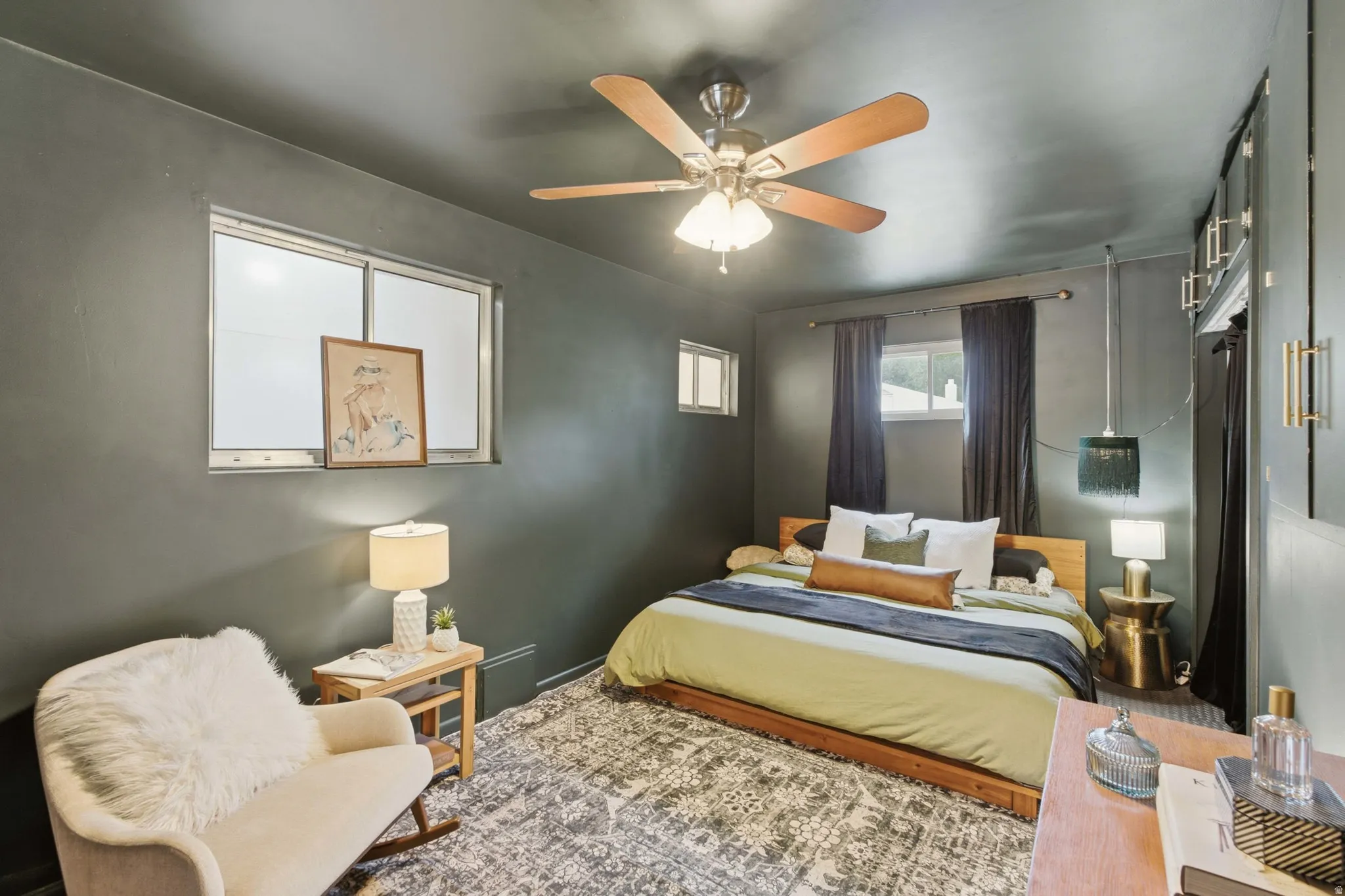 Bedroom featuring a ceiling fan with integrated lighting, multiple windows providing natural light, a built-in wall unit with cabinet doors.