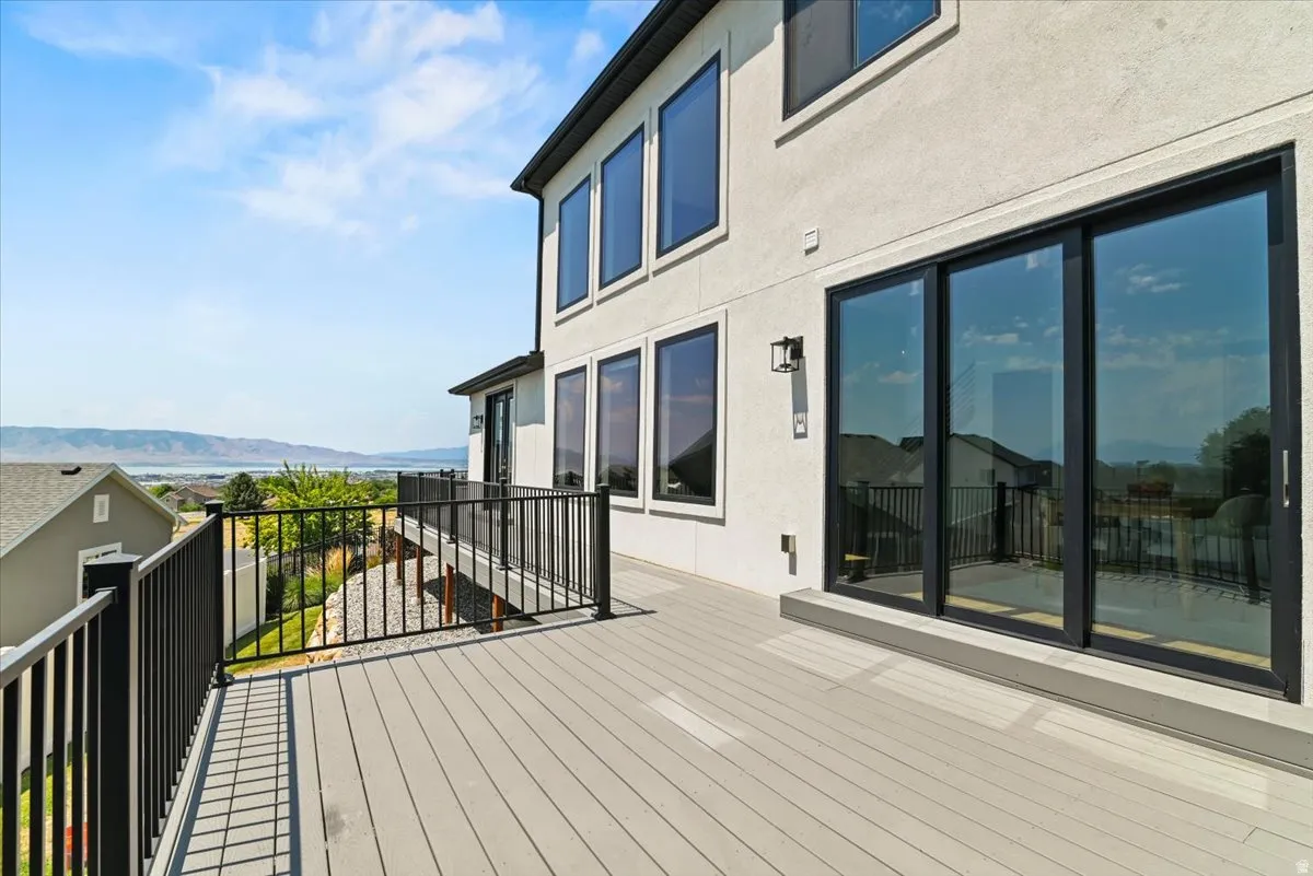 Expansive composite deck featuring light wood-finish decking, black aluminum railing with horizontal pickets, and direct access to the residence via multiple sliding glass doors